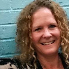 a woman with curly hair smiling in front of a blue wall and wearing a black shirt