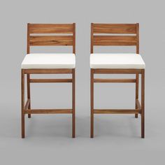 a pair of wooden chairs with white upholstered seat cushions and backrests