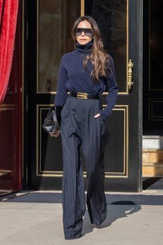 a woman standing in front of a door wearing black pants and a turtle neck sweater