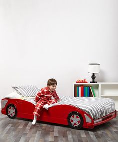 a young boy sitting on top of a red car bed in a room with white walls