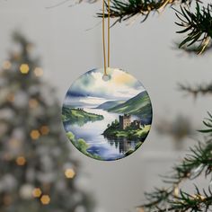 a christmas ornament hanging from a tree with a lake and castle on it