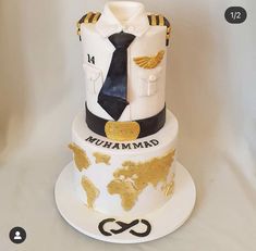 a white and black cake with gold trimmings on the bottom, topped by a navy uniform