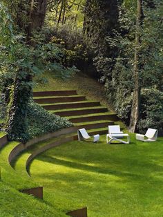 some white chairs sitting in the middle of a grass field with stairs leading up to it