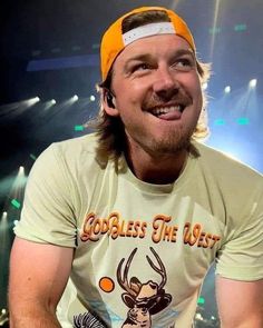 a man wearing a yellow hat smiles while sitting on a stool in front of a stage