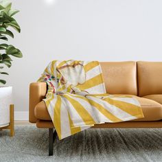 a couch with a yellow and white striped blanket on it next to a potted plant