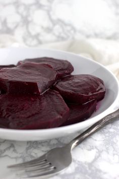 a white bowl filled with beets on top of a table next to a fork