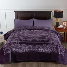 a bed with purple comforter and pillows on top of it, next to a night stand