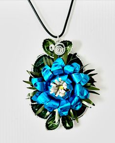 a blue flower is hanging from a black cord on a white surface with an ornament in the center