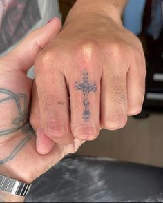 a man with a cross tattoo on his hand and wrist is holding onto another person's finger