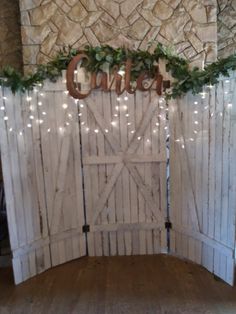 an open barn door decorated with greenery and lights that spell out the word comer