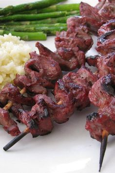 skewers of meat and rice on a plate with asparagus, broccoli