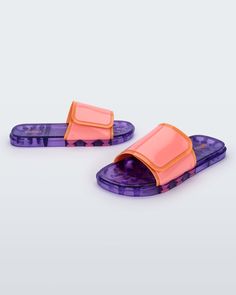 Daring and more sustainable, the Melissa Brave is a slide full of attitude and with a super unique design. The Velcro strap upper makes it practical to wear and the versions with a serigraph print make this slide even more stylish. Modern Pink Slides For Summer, Modern Slides For Spring Streetwear, Modern Slides With Translucent Outsole For Summer, Modern Slide Sandals For Streetwear, Orange Slides For Summer, Trendy Slides For Summer Streetwear, Trendy Summer Slides For Streetwear, Modern Adjustable Slides For Spring, Trendy Slides With Adjustable Strap For Vacation