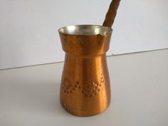 an old metal cup with a wooden spoon sticking out of it's side on a white surface