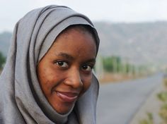 a woman with a scarf on her head smiles at the camera while standing in front of an empty road