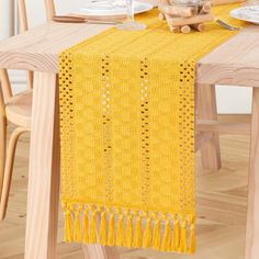 a yellow table runner on top of a wooden table with plates and utensils