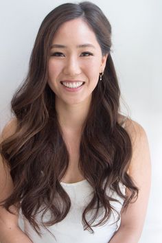 a woman with long brown hair smiling at the camera and wearing a white tank top