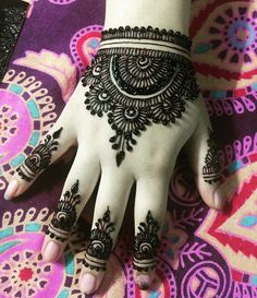 a woman's hand with henna tattoos on it, sitting on a colorful blanket