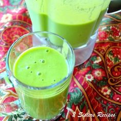 two glasses filled with green smoothies sitting on top of a colorful table cloth next to each other