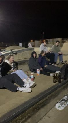 a group of people sitting on the side of a skateboard ramp at night time