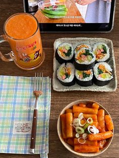 sushi and carrots are on the table next to a tablet with an orange juice