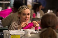 a woman sitting at a sewing machine working on her pink piece of clothing with other people in the background