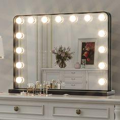 a white dresser topped with a large mirror and lots of lights on top of it