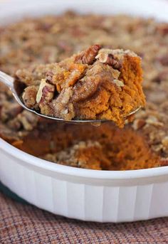 a spoon full of baked dessert in a white casserole dish on a table