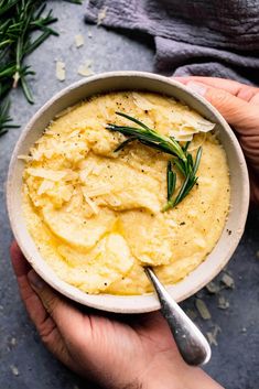 someone holding a bowl of mashed potatoes with rosemary