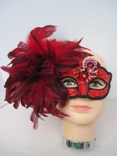 * Generous and red and black fluffy feathers over the right side of the face in this design. The feathers pick up the black braided trim around the mask and the black glitter eye liner. In addition the asymetrical faceted red crystal medallion adds more drama to the mask. * To secure the mask there are black satin ribbons to tie in the back of the head. The ribbons can be cut as I always include plenty of length. This mask will fit any size head and looks great on any age as well. * A great piec Mask With Feathers, Venetian Masquerade Masks, Feather Mask, Masked Ball, Venetian Masquerade, Glitter Eye, Back Of The Head, Satin Ribbons, Glitter Eyes