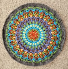 a crocheted round rug with an orange and blue flower design on the center