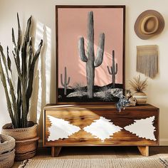 a living room with cactus plants and a painting on the wall next to a dresser