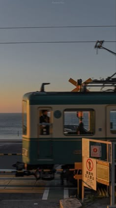 a train traveling down tracks next to the ocean at sunset with people standing on it