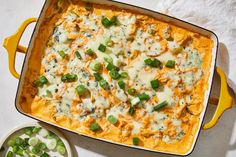 a casserole dish with green onions, cheese and sauce on it next to a bowl of peas