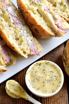 ham and cheese sandwich with mustard sauce on a white platter next to bread rolls