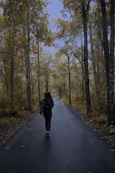 a person walking down a road in the middle of an autumn forest with leaves on the ground