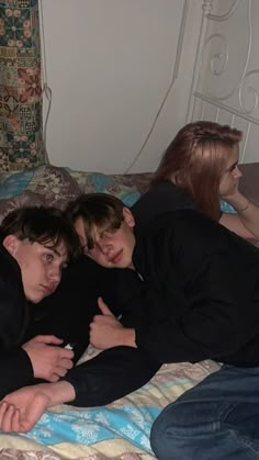 three people laying on a bed with one holding his arm around the other's head