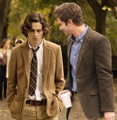 two young men are walking down the street, one is holding a coffee cup and talking to each other