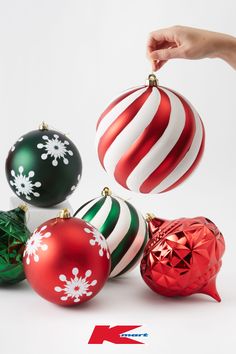 a hand is reaching for christmas ornaments on a white background with red, green and white stripes