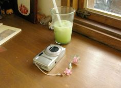 a camera and some green liquid sitting on a table next to a window sill