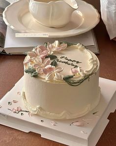 a white cake with flowers on it sitting on top of a table next to a cup and saucer