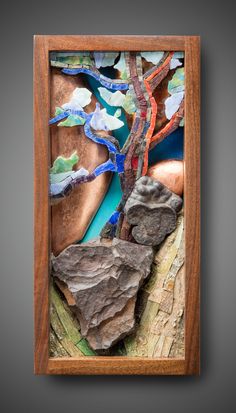 a wooden frame with some rocks and trees in it on a gray background, there is a blue stream running through the rock