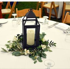 a candle is lit on top of a white table cloth with greenery around it