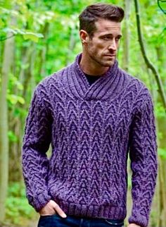 a man standing in the woods wearing a purple cabled sweater and dark blue jeans