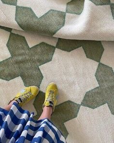 a person with yellow shoes is sitting on a green and white patterned blanket that looks like hexagonal shapes