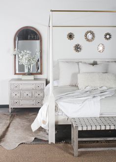 a white bed sitting in a bedroom next to a dresser with drawers and mirror on top of it