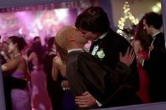 a man and woman kissing in front of a group of people at a formal event