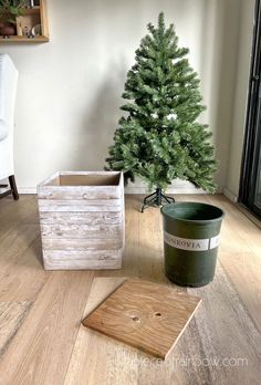 a small christmas tree sitting on top of a wooden floor next to a trash can