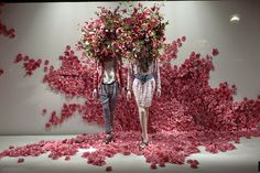 two mannequins with flowers on their heads in front of a white wall