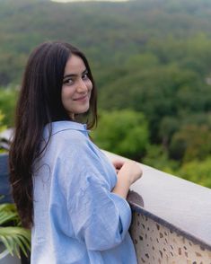 a woman standing on top of a balcony next to a lush green forest covered hillside