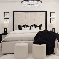 a white bedroom with black and white accessories on the bed, chandelier and ottomans